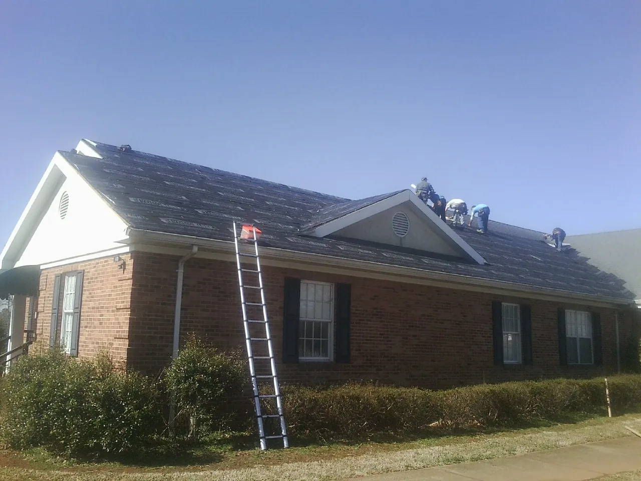 Crew tearing shingles off a brick ranch roof with a ladder set — Emergency Roof Repair work by our crew in Indianola
