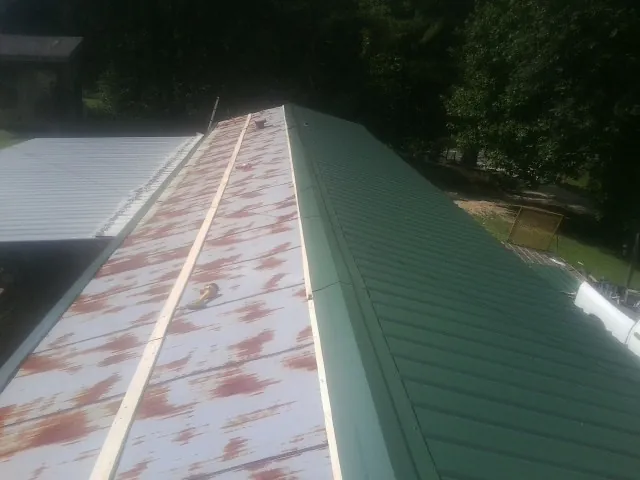 Old rusted panels beside newly installed green metal roofing — Wind Damage Roof Repair by Roofing Brothers in Indianola
