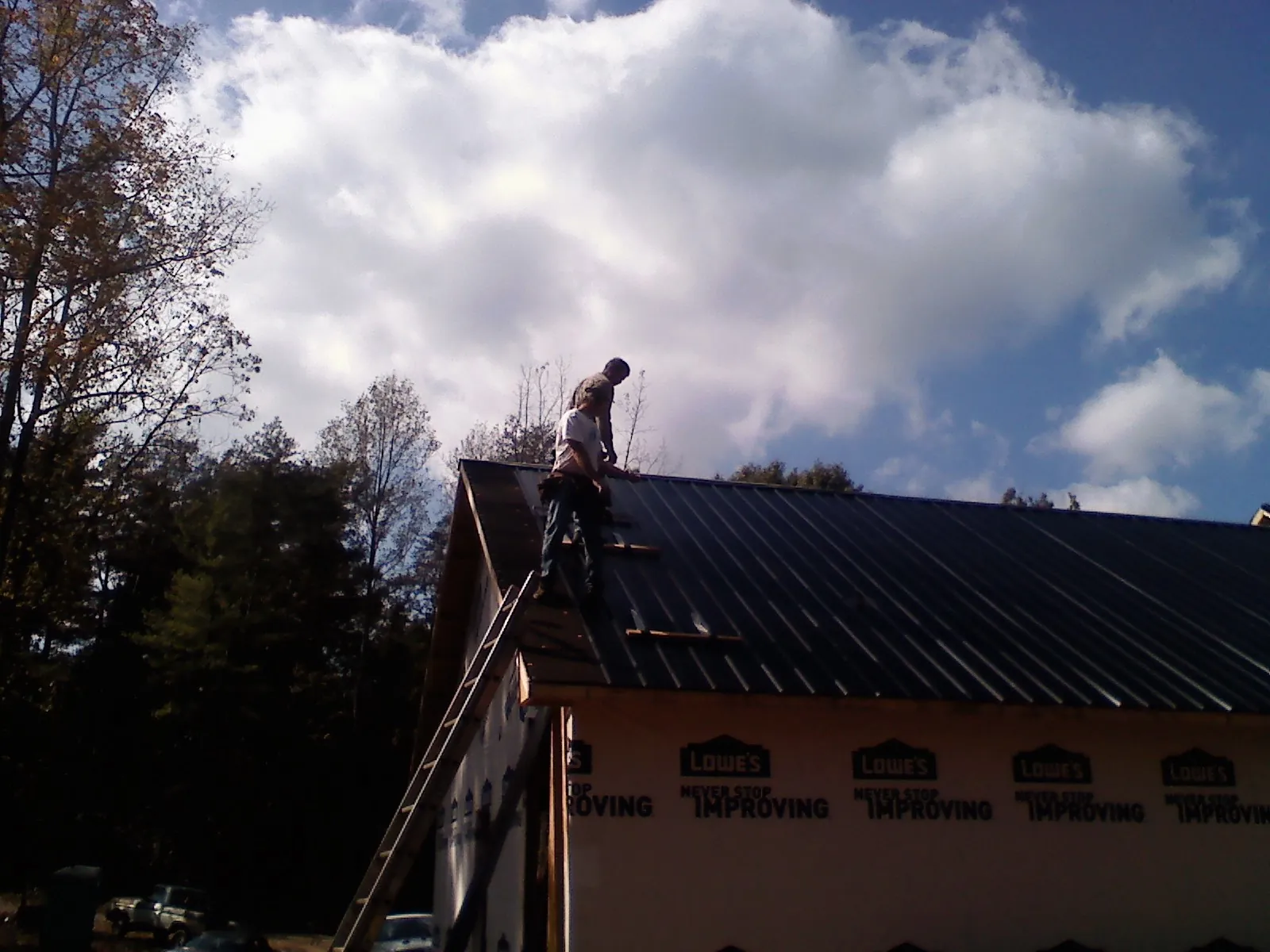 Roofer fastening dark metal panels high against a cloudy sky, from a Roof Inspection job in Indianola