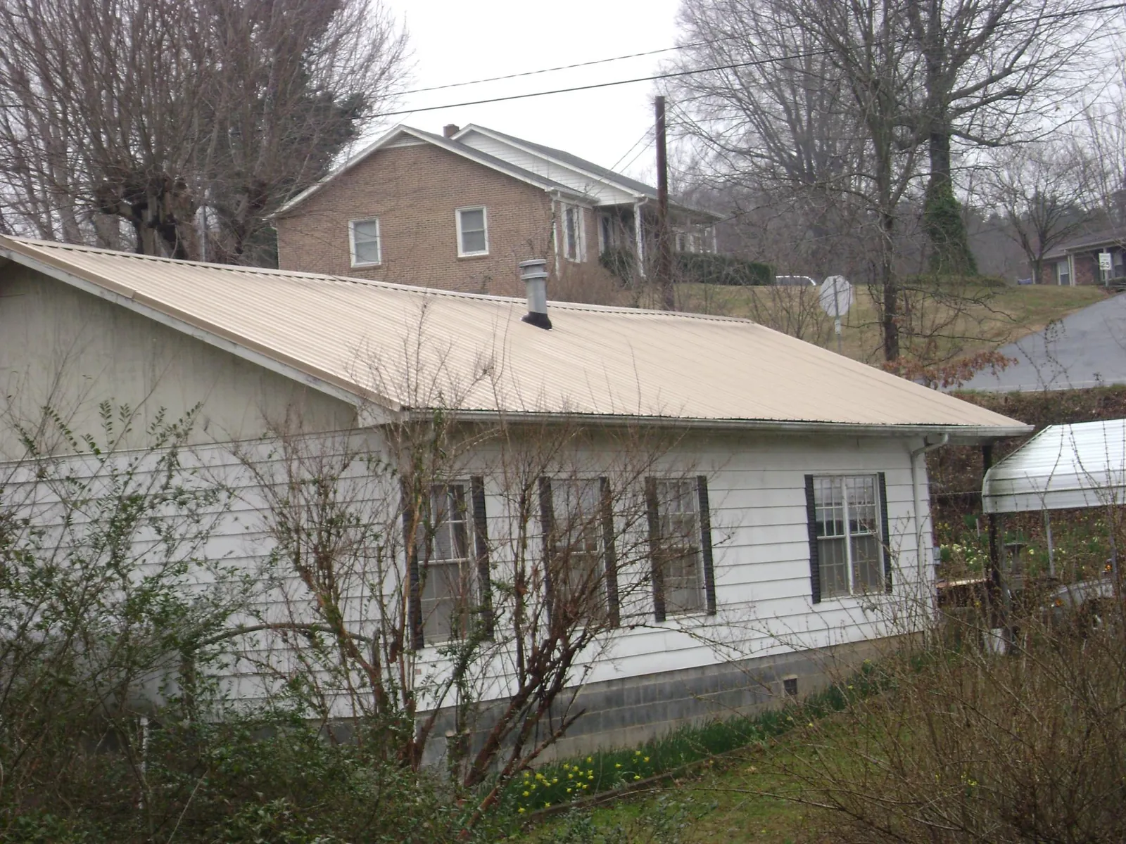 Tan metal roof on a white sided house set into a hillside — Commercial Roofing by Roofing Brothers in Indianola