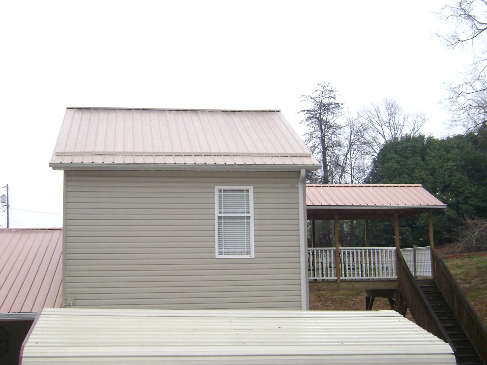 Tan metal roofs on a two story addition and attached porch, from a Roof Replacement job in Indianola